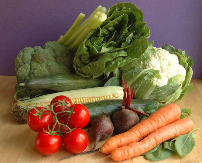 Et træbord fyldt med lækre friske grøntsager: broccoli, majskolbe, blomkål, tomater, rødbeder, selleri, gulerødder, squash og romaine salat.