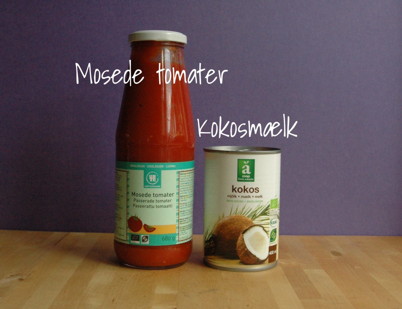 En flaske med mosede tomater samt en dåse kokosmælk begge økologiske og stående på et træbord.