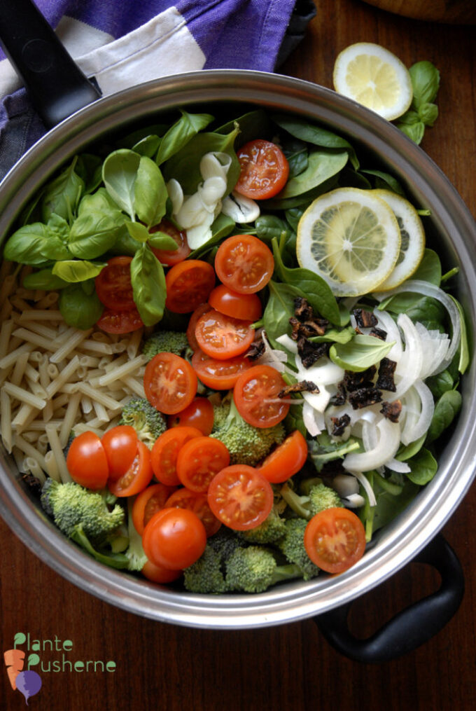 Stor pande med ingredienser til vegansk og vegetarisk one pot pasta på en træbordplade. Fyldt med grøn spinat og pasta