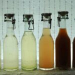 6 flasker hyldeblomst i forskellige nuancer oplyst bagfra