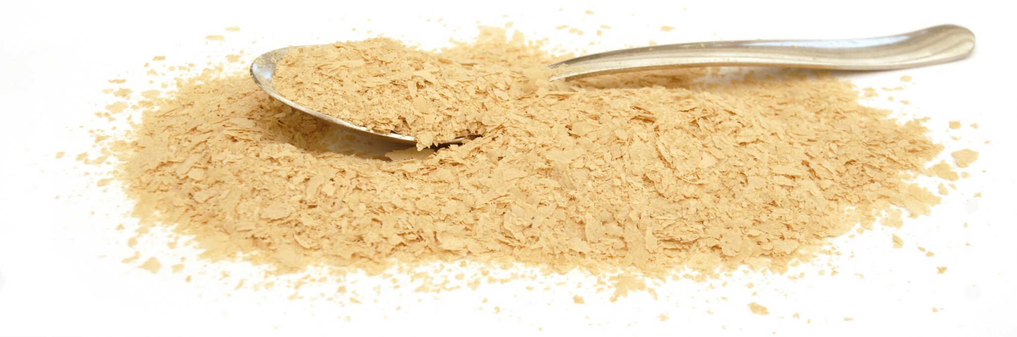 Nærbillede af gærflager drysset udover en ske på hvid baggrund