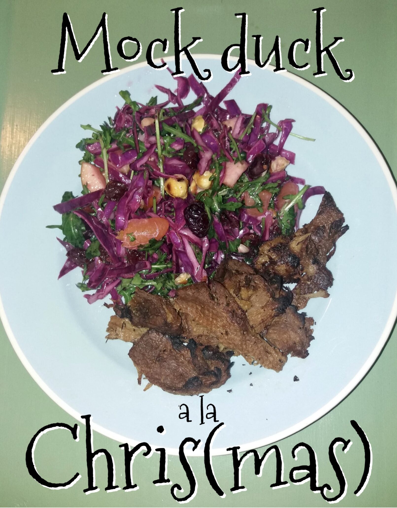 På en grøn baggrund står en lyseblå tallerken anrettet med en smuk salat i mange farver og en portion Vegansk and også kendt som mock duck. Henover billedet står der skrevet Mock duck a la Chris parentes mas